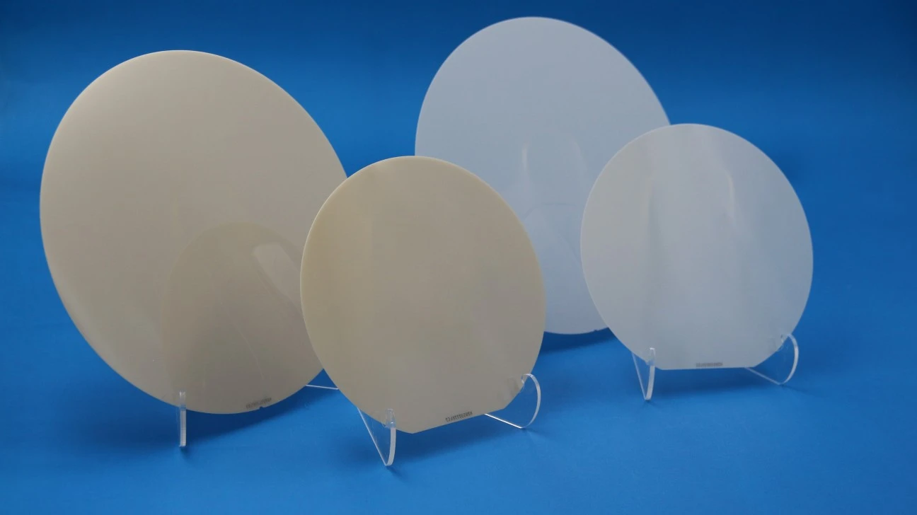 Four wafer-sized aluminum nitride technical-ceramic wafers in 6-inch and 8-inch formats displayed on clear stands.